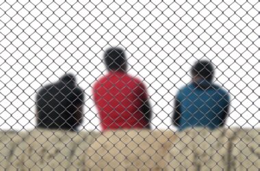 Migrantes de espaldas tras una valla