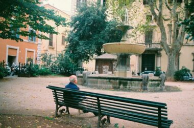 persona mayor sentada en un banco en una plaza vacía