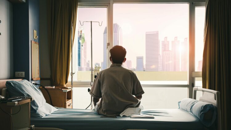 hombre de espaldas sentado en una habitación de un hospital mira a través de una ventana