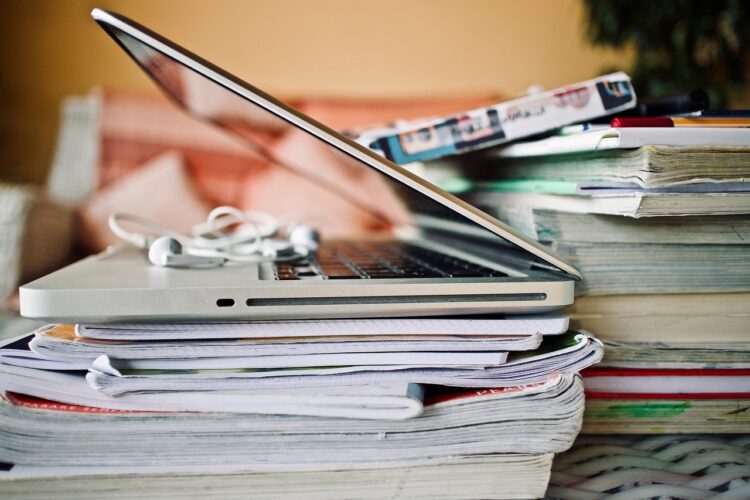 Un portátil sobre una pila de libros y revistas