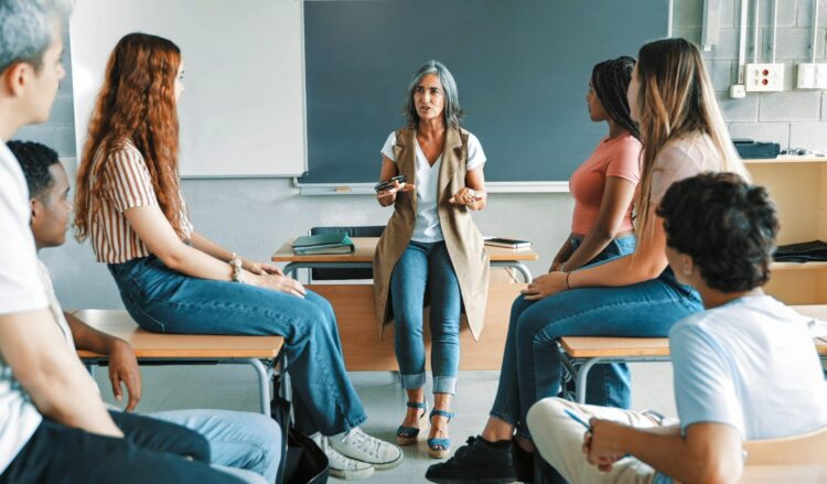 un grupo de alumnos y alumnas en un aula en torno a una profesora