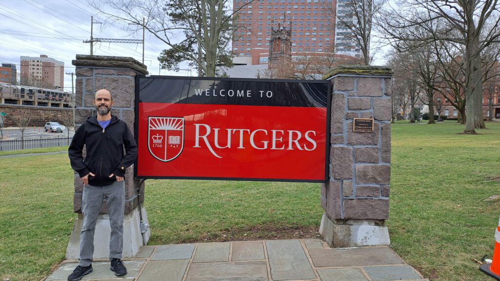 El conferenciante ante un cartel grande de la universidad que dice: Welcome to Rutgers.