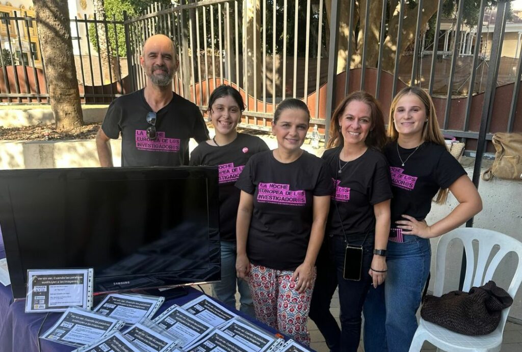 Investigadoras del grupo y voluntarias posando frente a la mesa del taller con las camisetas del evento